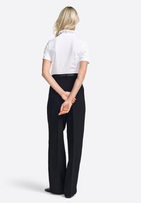 Bela srajca s kratkimi rokavi in naborkanim ovratnikom, v kombinaciji z visokim pasom črnimi hlačami. Obleka je prikazana s hrbtne strani.