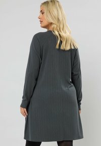 Abito a coste grigio scuro con maniche lunghe, orlo arrotondato e vestibilità rilassata. Realizzato in un tessuto morbido con texture verticale.