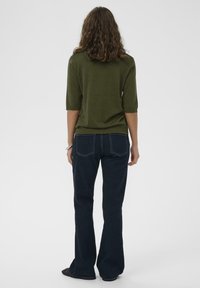 Maglione verde oliva a maglia con maniche a lunghezza 3/4, abbinato a jeans svasati blu scuro con tasche posteriori e cuciture a contrasto.