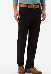 Pantaloni neri in cotone, design a gamba dritta, abbinati a una cintura in pelle marrone e scarpe eleganti marroni. La texture appare liscia e strutturata.
