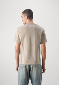 Camiseta de algodón beige de manga corta, con un cuello redondo clásico y un ajuste relajado, combinada con jeans azul desgastado.