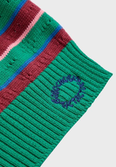 Bonnet en tissu tricoté avec des rayures vertes, roses et bordeaux. Présente une texture côtelée et un logo circulaire brodé en bleu.