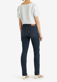 Blusa azzurro chiaro a maniche a sbuffo, abbinata a jeans blu scuro con design della tasca posteriore ricamato e etichetta in tono chiaro sulla vita.