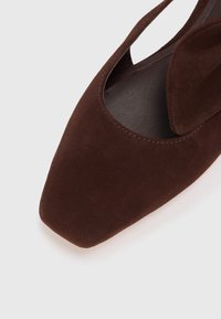 Brown suede slingback shoe with a pointed toe, featuring a cutout design and a smooth, textured insole. Simple stitching detail visible.