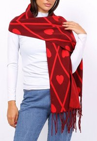 Écharpe rouge et bordeaux dotée d'un motif de diamant avec des cœurs rouges. Texture douce avec des extrémités frangées, drapée sur un top blanc.