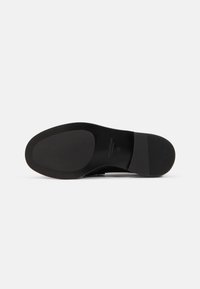 Semelle de chaussure en cuir noir avec une forme lisse et arrondie. Présente une surface plate et texturée ainsi qu'un talon cranté pour une meilleure adhérence.