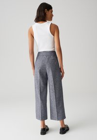 Pantalons à jambes larges en tissu texturé bleu et gris, avec une taille haute et des poches arrière. Assortis à un haut sans manches blanc.