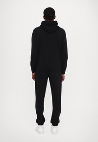 Black hoodie and sweatpants set, featuring a relaxed fit, textured fabric, ribbed cuffs, and a large hood, worn with white sneakers.