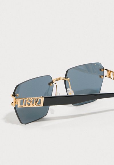 Occhiali da sole neri in plastica con dettagli in metallo dorato, lenti scure a forma quadrata e un logo audace sulla aste. Inclusi naselli trasparenti.