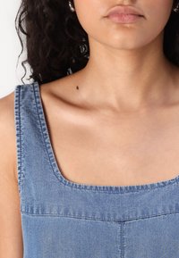 Lyseblå denimtop med brede stropper, firkantet utringning og en glatt tekstur. Har synlige stikninger og et rent, minimalistisk design.