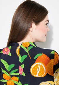 Vestido con estampado floral que presenta vibrantes tonos de naranja, verde y rosa sobre un fondo oscuro; tejido suave con un escote redondeado y mangas cortas.