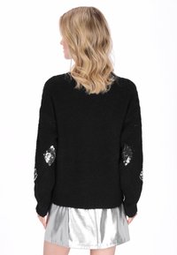 Fekete kötött pulóver laza szabással, ujjain flitteres rombusz díszítéssel. Ezüstösen csillogó szoknyával párosítva.