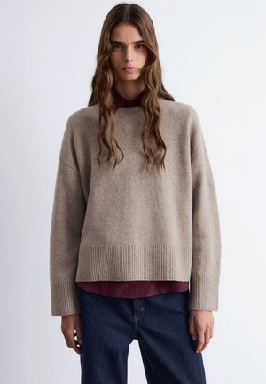 Beige gestrickter Pullover mit geripptem Saum und Bündchen, in lässiger Passform und mit Rundhalsausschnitt. Über einem burgunderfarbenen Hemd mit Kragen getragen.