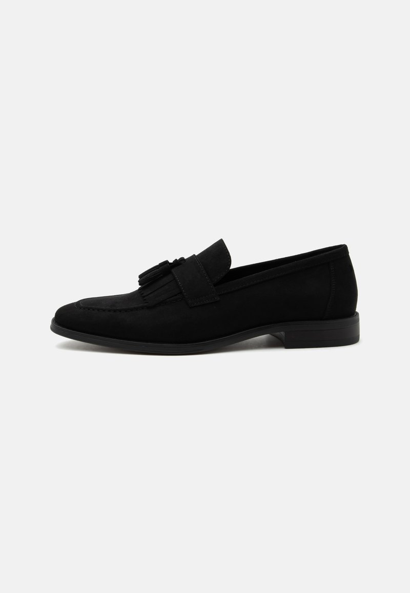 Mocassin en cuir noir avec petit talon, bout arrondi et pompons décoratifs sur le dessus, présenté en profil latéral sur fond blanc.