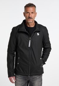 Zwarte zip-up jack met een hoge kraag, voorzien van een logo op de linkerkant van de borst, zilverkleurige hardware en zijzakken met drukknoopsluitingen.