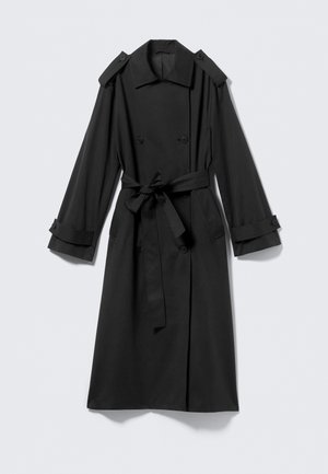 Svart ankel-langt trenchcoat laget av glatt stoff. Har dobbel-breasted front, brede klaffer, skulderepauletter, og en knytbelte.