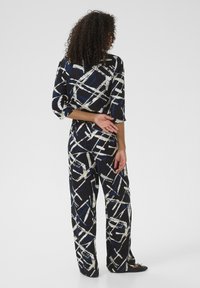 Navy jumpsuit with abstract white and blue patterns, featuring three-quarter sleeves, wide legs, and a relaxed fit, made of lightweight fabric.