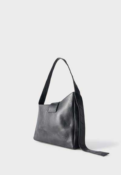 Μαύρη δερμάτινη τσάντα ώμου με φαρδιά λουρί και καπάκι, τοποθετημένη όρθια σε απλό λευκό φόντο.