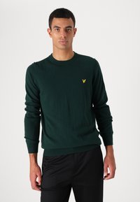 Suéter de malha verde escuro com mangas longas, decote redondo e um pequeno logótipo amarelo no lado esquerdo do peito. Textura suave e design ajustado.