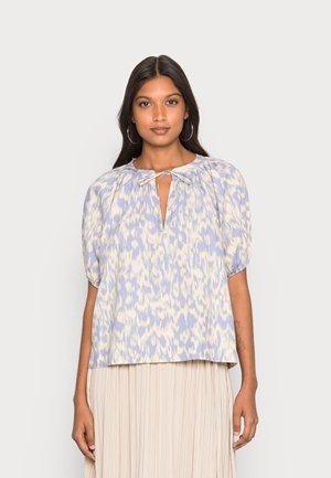 Blusa azul claro com um padrão abstrato creme, mangas curtas em balão, decote redondo e uma abertura em forma de chave com detalhe de laço.