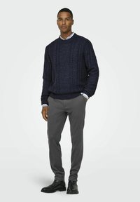 Pull en maille côtelée marine à col rond, associé à un pantalon gris slim et des bottines noires. Design classique en tricot texturé.