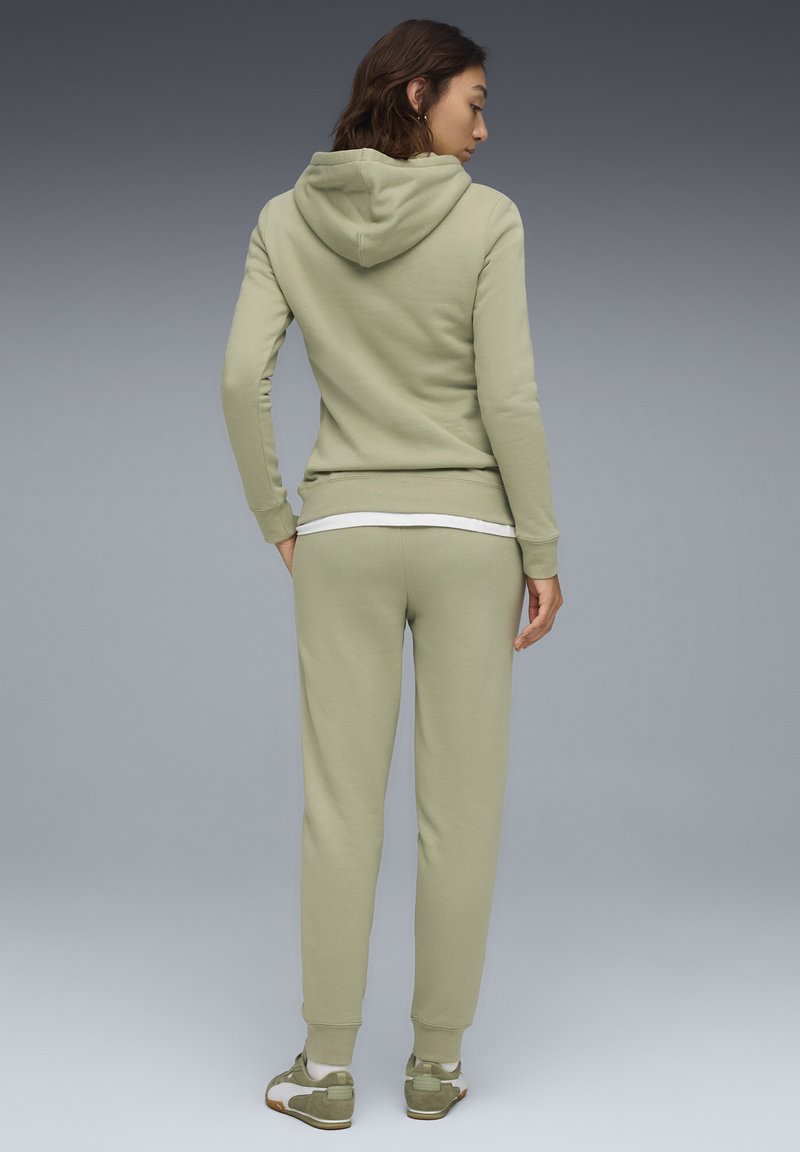Lys grøn hættetrøje med hætte og forlommer, parret med matchende sweatpants. Fremstillet af blødt stof, tætsiddende design og ribbede manchetter.