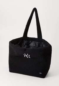 Μαύρη τσάντα tote με βελούδινη, υφή στην εξωτερική επιφάνεια, που διαθέτει αντίθετο άσπρο λογότυπο. Διπλές λαβές και ευρύχωρος μαύρος εσωτερικός χώρος.