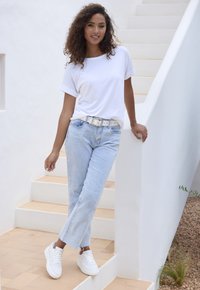 Weißes T-Shirt mit kurzen Ärmeln kombiniert mit hellblauen, lockeren Jeans und weißen Sneakern, ausgestattet mit einem dekorativen weißen Gürtel und strukturiertem Stoff.