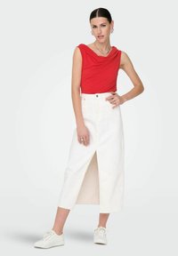 Haut drapé rouge et jupe blanche mi-longue avec fente à l'avant, accompagnés de baskets blanches. Tissu lisse, design simple, look décontracté.