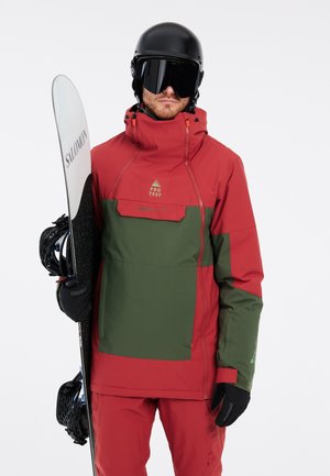 Rode en groene snowboardjas met een hoge kraag, een ritszak en verstelbare manchetten, gecombineerd met rode broeken en zwarte handschoenen.