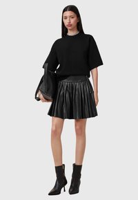Suéter negro de gran tamaño, falda corta de cuero con pliegues, botas negras de tacón alto hasta la rodilla, con un bolso negro a juego, que cuenta con cremalleras y una textura suave.