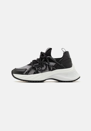 Scarpa sportiva nera e grigia con tomaia in rete, suola spessa bianca e suola esterna in gomma nera. Presenta lacci e un anello di presa sul tallone.