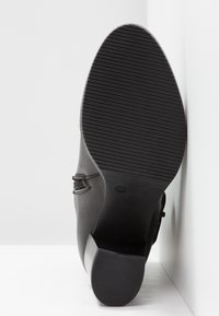 Botín negro con suela de goma texturizada, tacón bajo y diseño curvado en los laterales. Presenta detalles cosidos a lo largo de la parte superior. Talla 37.