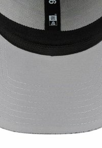 Unterseite eines hellgrauen Kappen- schirms mit schwarzem Innenfutter und einem schwarzen Größenetikett, das mit "9" und dem "New Era"-Logo beschriftet ist.