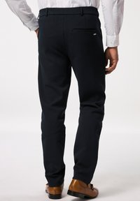 Pantaloni navy scuri con una vestibilità slim, dotati di una tasca posteriore e una texture liscia. Indossati con scarpe eleganti marroni.