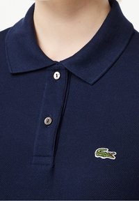 T-shirt polo bleu marine en tissu tissé texturé ; doté d'un col classique, de deux boutons et d'un logo crocodile brodé en vert.