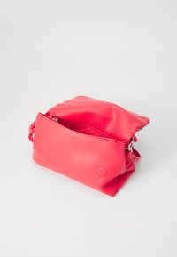 Borsa in pelle sintetica rosa con chiusura a zip, forma arrotondata e due accenti circolari sul fronte. Texture morbida, design informale.
