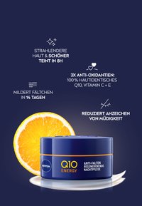 Runder blauer Behälter mit orangefarbenen Akzenten, beschriftet mit "Q10 ENERGY", enthält eine anti-aging Nachtcreme. Eine frische Orangenscheibe liegt daneben.