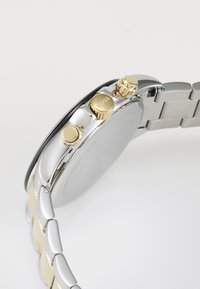 Stainless steel watch with silver and gold accents. Features a round case, three push buttons, and a linked bracelet design.