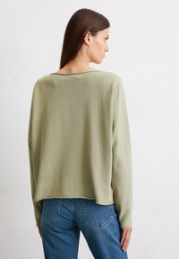 Hellgrüner Langarmpullover mit lässiger Passform, weitem Ausschnitt und abgerundetem Saum, kombiniert mit blauen Jeans. Weiches, strukturiertes Material.
