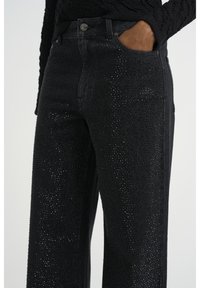 Vaqueros negros con un diseño de pierna ancha, adornados con un patrón de pequeños y brillantes tachuelas. Fabricados con denim de acabado texturizado.