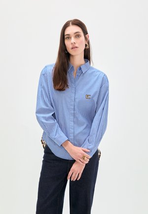 Camisa de rayas azul claro y blanca hecha de algodón con cuello y cierre de botones. Cuenta con un logo bordado en el pecho.
