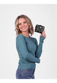 Teal ribbed sweater with long sleeves, paired with blue jeans, holding a black wallet featuring pink dots and a gold snap closure.