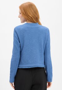 Blau strukturierte Jacke mit langen Ärmeln und einem Fransen-Saum. Sie hat einen runden Halsausschnitt und eine leicht lockere Passform und besteht aus Strickmaterial.
