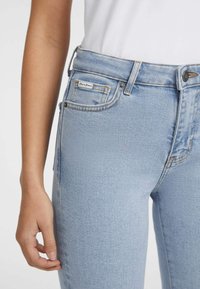 Ljusblå denimjeans med hög midja, femfickorsdesign och en liten logg på höger framficka. Slät textur.