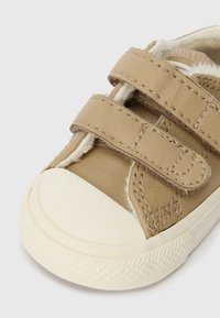 Brūnas ādas bērnu kurpes ar diviem Velcro aizdariem, noapaļota purngala forma, balta gumijas zole un mīksts apšuvums, kas redzams pa malām.