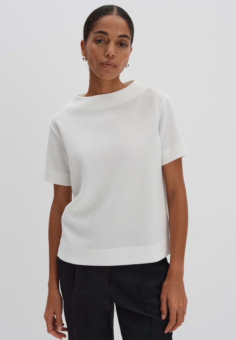 White textured short-sleeve top with a round neckline, featuring a ribbed pattern. Paired with black tapered pants. Simple and minimalistic design.