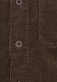 Närbild av brun manchester med vertikala ribbor, bruna knappar och en sydd ficka på höger sida.