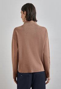 Ljust brunt, långärmad tröja med en mjuk textur, avslappnad passform och ett subtilt ribbat mönster på baksidan. Kombinerad med marinblå byxor.