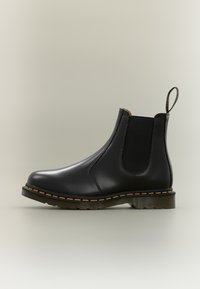 Bota Chelsea preta em couro com painéis laterais elásticos, costura amarela e sola de borracha texturizada. Possui uma aba para puxar na parte de trás.